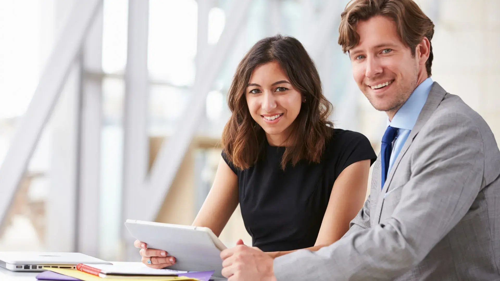 A man and a woman in corporate attire discussing something over a tablet