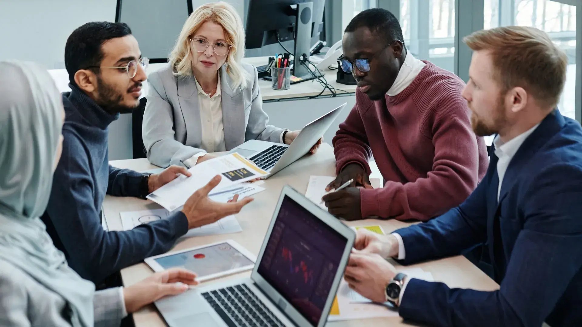A group of office professionals in an intent discussion over laptop and papers, presumably talking about data breaches
